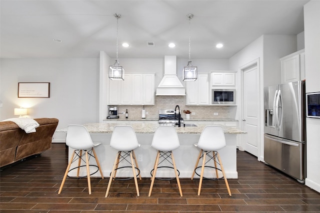 kitchen with wood tiled floor, decorative backsplash, custom exhaust hood, stainless steel appliances, and a sink