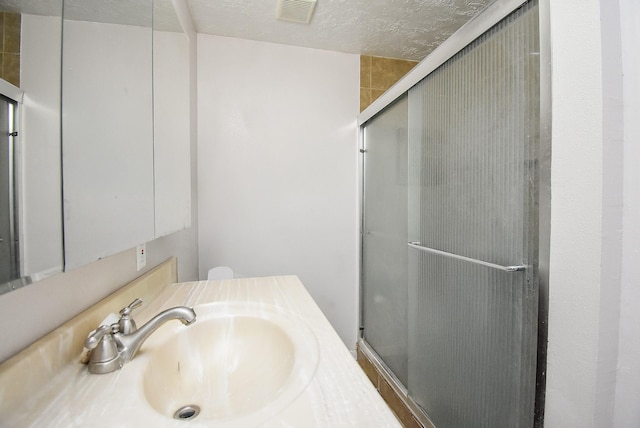 bathroom with a textured ceiling, vanity, a shower stall, and visible vents