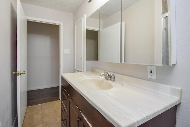 bathroom with baseboards, vanity, a textured ceiling, and tile patterned floors