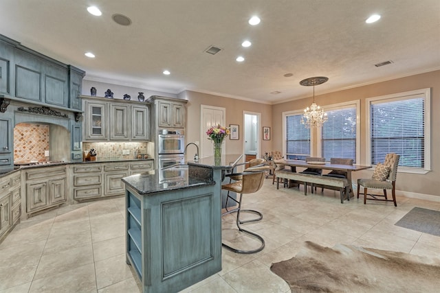 kitchen with a breakfast bar, visible vents, backsplash, ornamental molding, and an island with sink