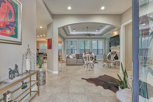 interior space featuring arched walkways, a fireplace, a raised ceiling, and a ceiling fan