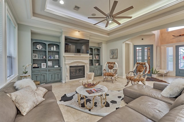 living room with built in features, a tray ceiling, arched walkways, crown molding, and visible vents