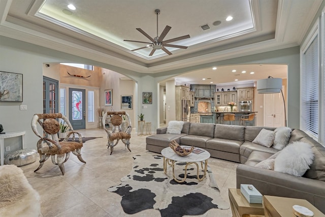 living area with arched walkways, recessed lighting, visible vents, ornamental molding, and a raised ceiling