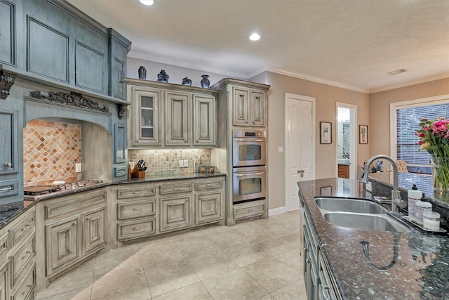 kitchen with a sink, ornamental molding, appliances with stainless steel finishes, backsplash, and dark stone counters