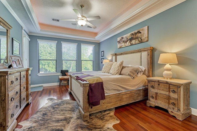 bedroom featuring ornamental molding, a tray ceiling, visible vents, and dark wood finished floors