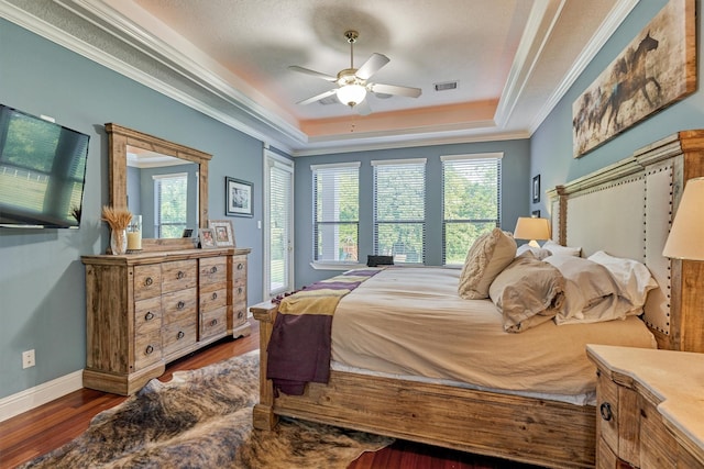 bedroom with a raised ceiling, visible vents, ornamental molding, wood finished floors, and baseboards