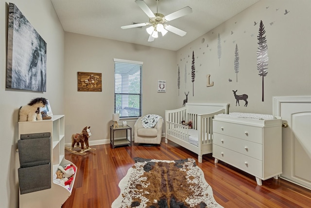 bedroom with ceiling fan, a crib, baseboards, and wood finished floors