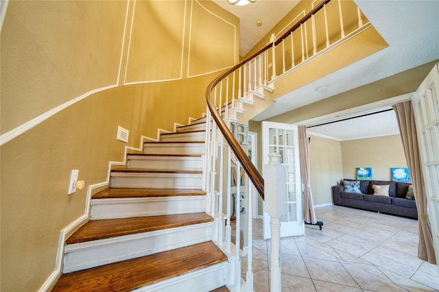 stairs featuring baseboards, ornamental molding, a high ceiling, and tile patterned floors