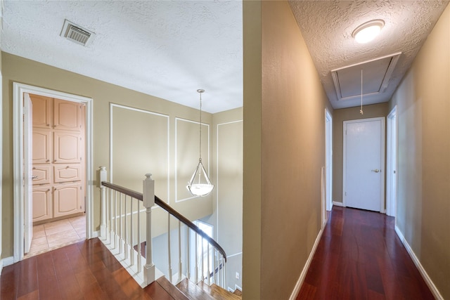 corridor with visible vents, wood finished floors, an upstairs landing, and attic access