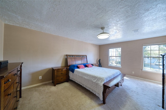 bedroom featuring light carpet, visible vents, baseboards, and a textured ceiling