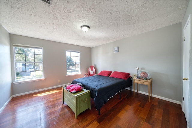 bedroom with a textured ceiling, wood finished floors, visible vents, and baseboards