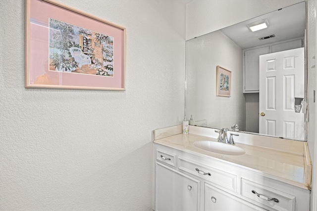 bathroom with visible vents, a textured wall, and vanity