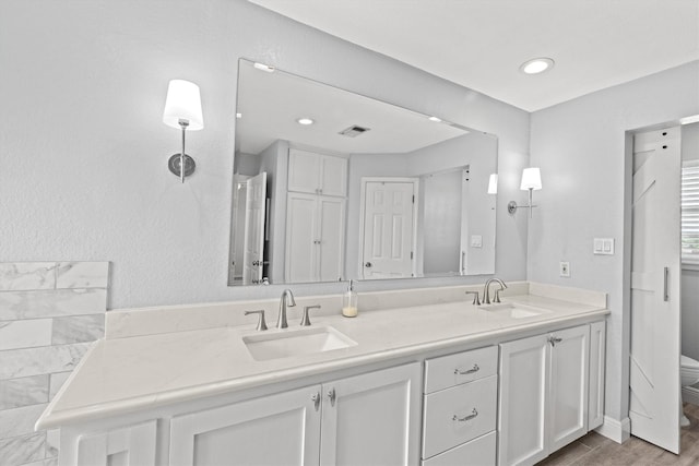 bathroom featuring wood finished floors, visible vents, a sink, and double vanity