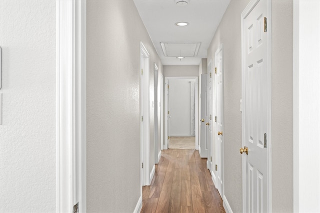 corridor featuring wood finished floors, attic access, and baseboards