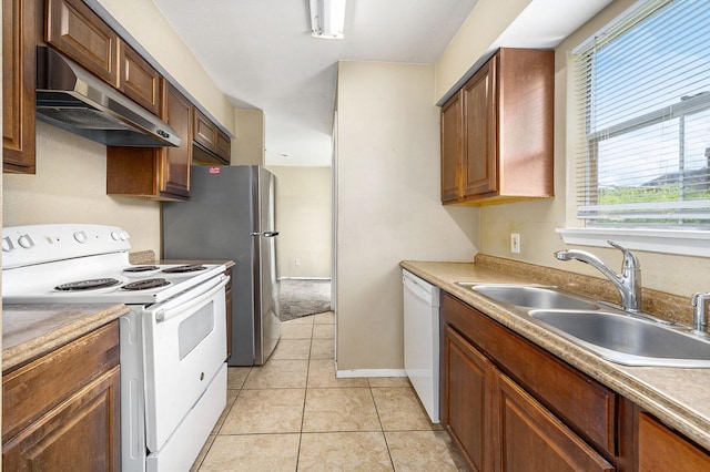 kitchen featuring light tile patterned flooring, under cabinet range hood, white appliances, a sink, and baseboards