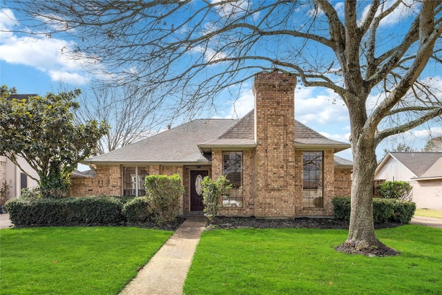 view of front facade with a shingled roof, a front yard, brick siding, and a chimney