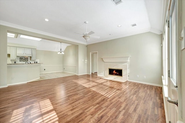 unfurnished living room with visible vents, a fireplace with flush hearth, ornamental molding, light wood-type flooring, and ceiling fan with notable chandelier