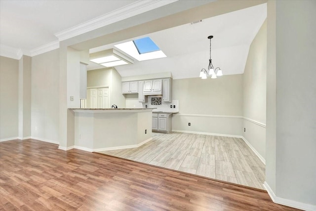 kitchen featuring light wood-style floors, vaulted ceiling with skylight, light countertops, and crown molding