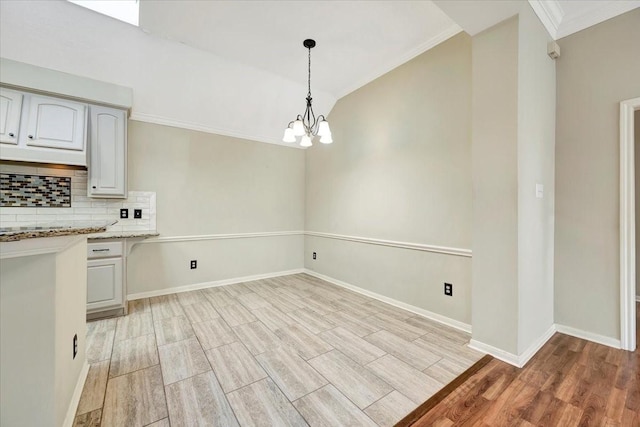 unfurnished dining area featuring crown molding, lofted ceiling, light wood-style flooring, a chandelier, and baseboards