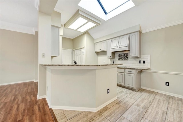 kitchen featuring a peninsula, backsplash, baseboards, and light stone countertops