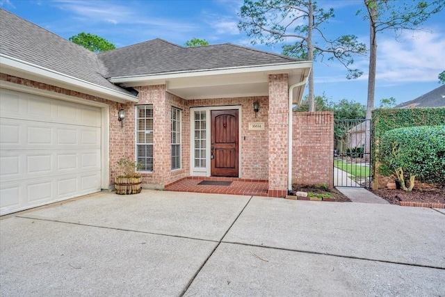 doorway to property with driveway, a shingled roof, an attached garage, fence, and brick siding