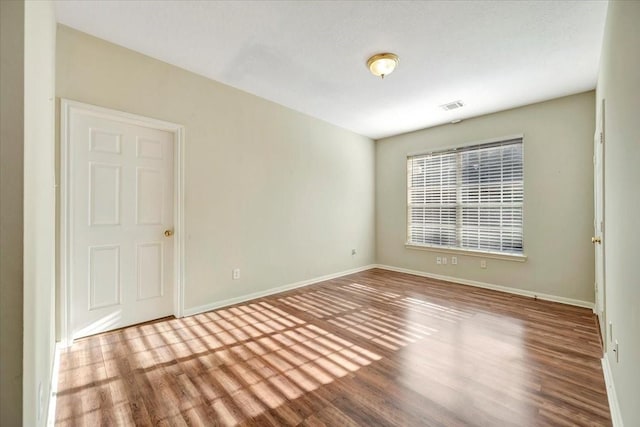 empty room featuring wood finished floors, visible vents, and baseboards