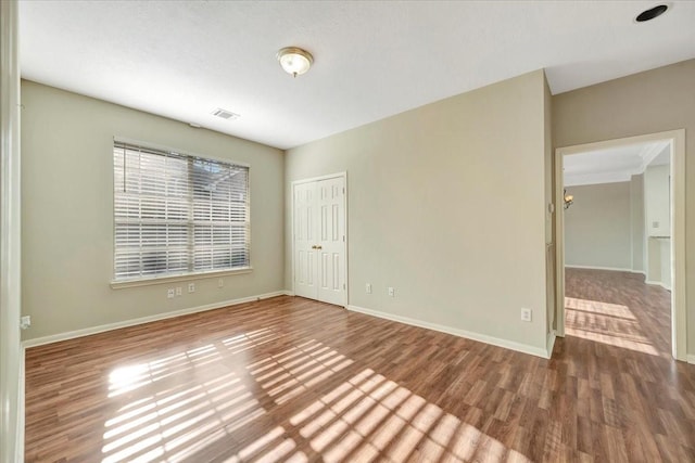 empty room with baseboards, visible vents, and wood finished floors