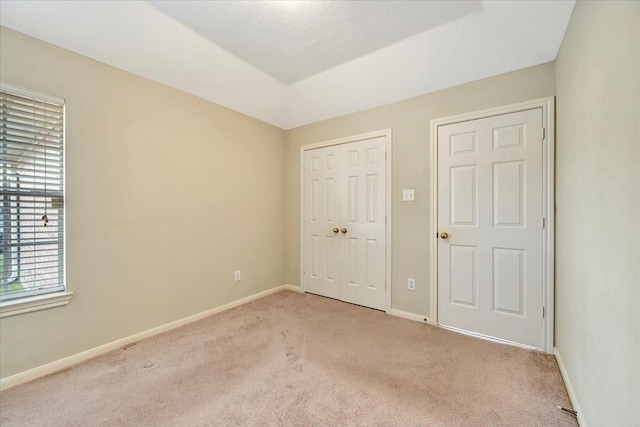 unfurnished bedroom with a closet, light carpet, and baseboards