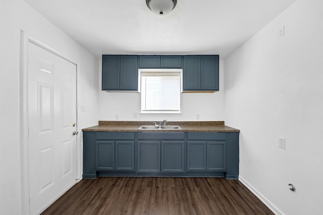 kitchen with dark wood finished floors, dark countertops, a sink, blue cabinets, and baseboards