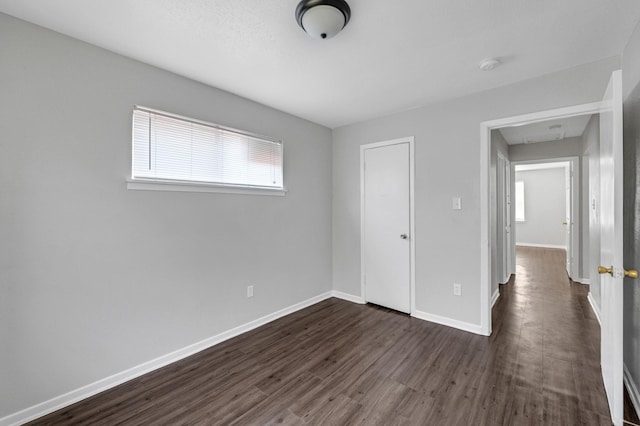 unfurnished bedroom with attic access, dark wood finished floors, and baseboards