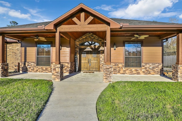 doorway to property featuring a yard, stone siding, a shingled roof, and a ceiling fan