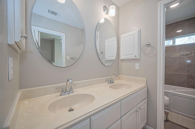 bathroom featuring toilet, double vanity, a sink, and visible vents