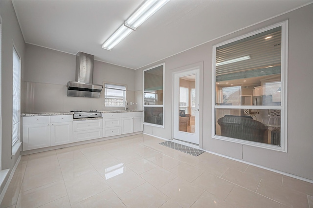 kitchen with white cabinetry, a sink, light tile patterned flooring, stovetop, and wall chimney exhaust hood