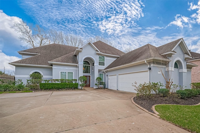 view of front of home with concrete driveway, roof with shingles, an attached garage, fence, and stucco siding