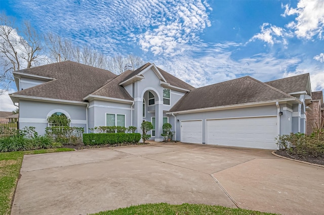 traditional home featuring a garage, driveway, a chimney, and stucco siding