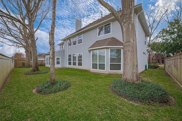 rear view of house with a chimney, stucco siding, a shingled roof, a lawn, and a fenced backyard