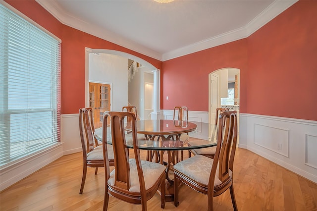 dining space with arched walkways, a wainscoted wall, and light wood-style floors