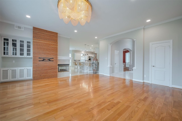 unfurnished living room featuring arched walkways, crown molding, light wood-type flooring, and an inviting chandelier