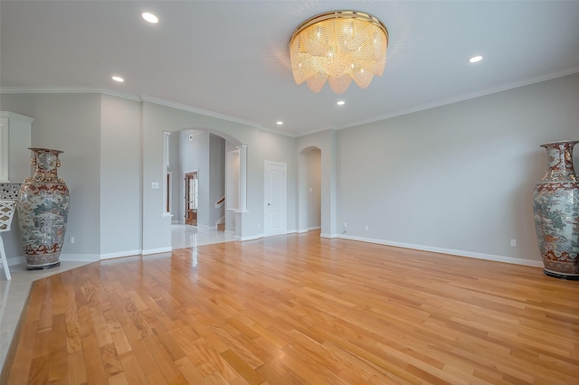 spare room featuring arched walkways, recessed lighting, light wood-type flooring, and baseboards