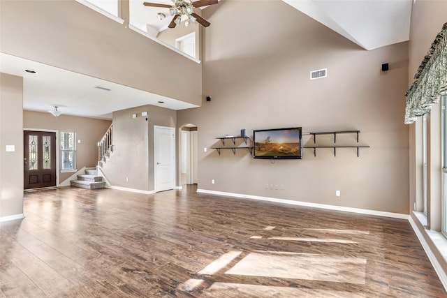 unfurnished living room with arched walkways, wood finished floors, visible vents, baseboards, and stairway