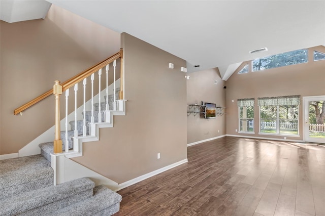 living room with a towering ceiling, wood finished floors, visible vents, and baseboards