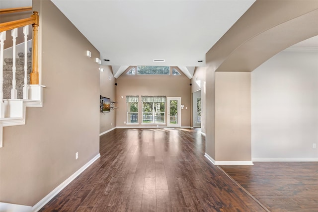 interior space featuring arched walkways, a high ceiling, wood finished floors, baseboards, and stairs