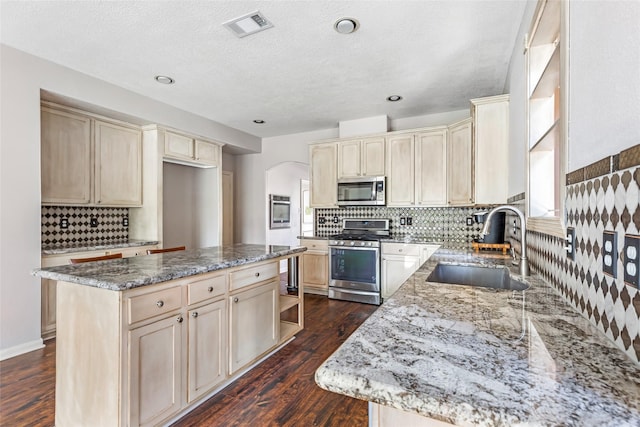 kitchen featuring visible vents, appliances with stainless steel finishes, cream cabinets, open shelves, and a sink