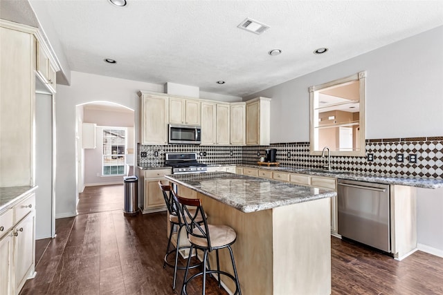 kitchen with arched walkways, visible vents, stainless steel appliances, cream cabinetry, and a sink