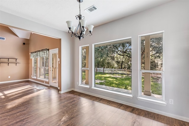 unfurnished dining area featuring baseboards, wood finished floors, visible vents, and a notable chandelier