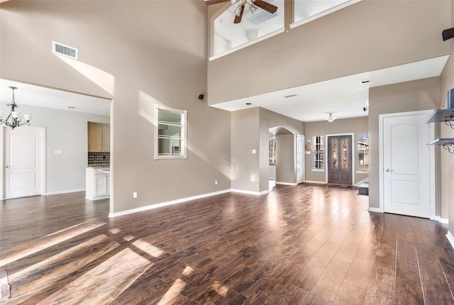 unfurnished living room featuring visible vents, arched walkways, dark wood-type flooring, and ceiling fan with notable chandelier