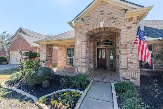 doorway to property featuring covered porch, brick siding, and roof with shingles