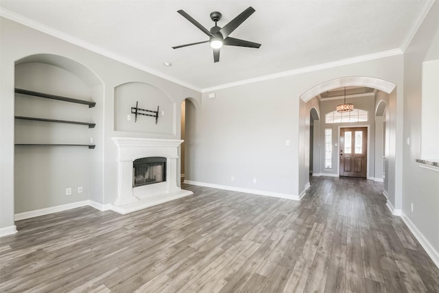 unfurnished living room featuring a fireplace with raised hearth, ornamental molding, wood finished floors, and baseboards