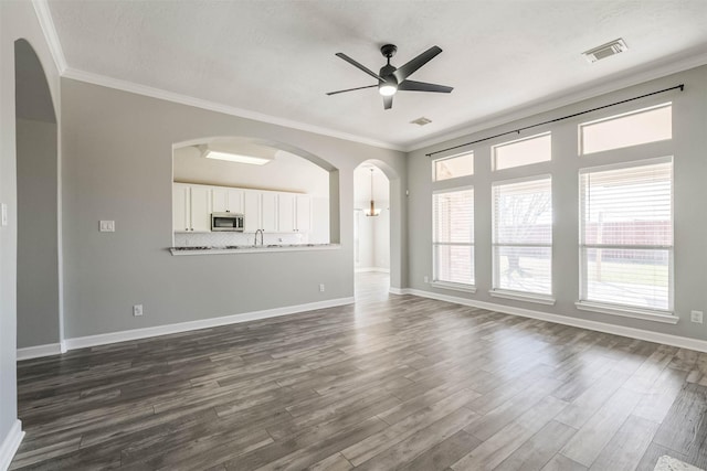 unfurnished living room with dark wood-style floors, baseboards, visible vents, and ornamental molding