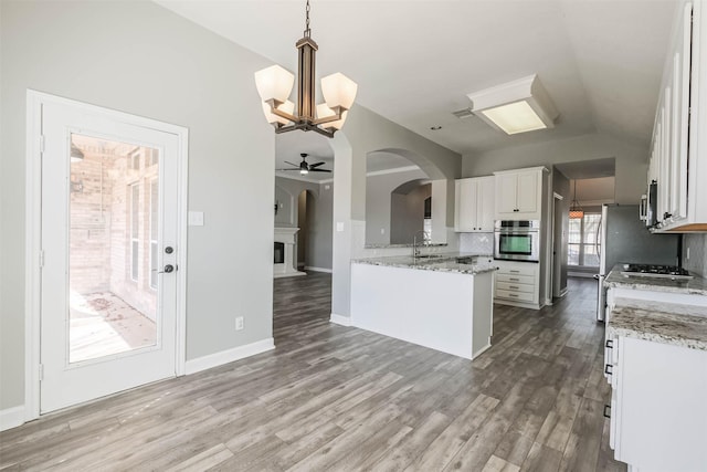 kitchen with stainless steel appliances, wood finished floors, white cabinets, vaulted ceiling, and decorative backsplash